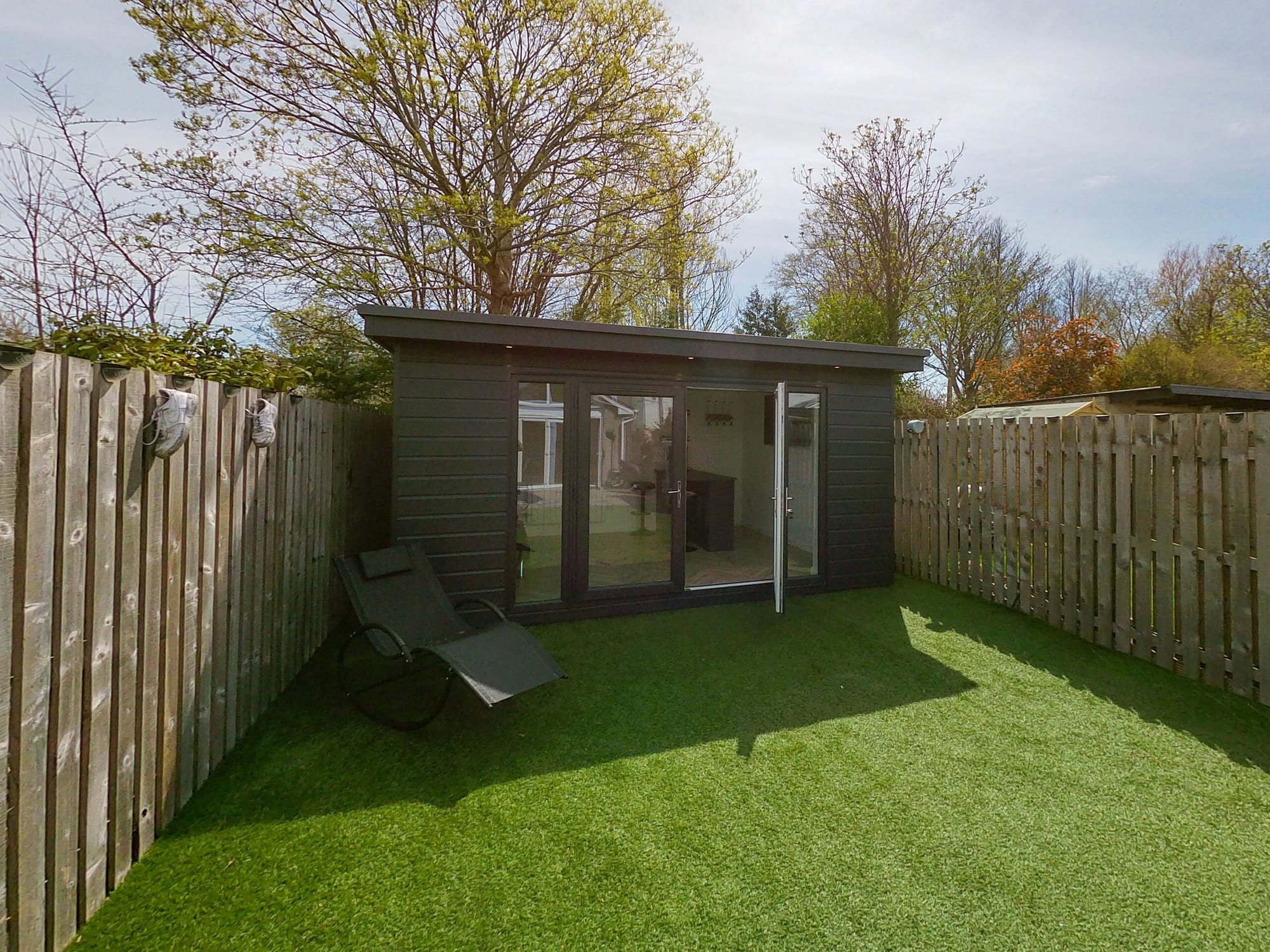 Exterior photo of a contemporary timber-clad garden room with large glazed doors, set on a patio in a residential garden.